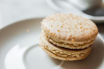 Fototapeta na wymiar A close up photo of a macaron with salted caramel on a white saucer, a cup of coffee in the background