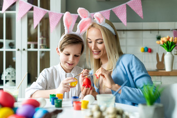 Obraz na płótnie Canvas Happy mother and son wearing in bunny ears preparing to Easter and painting eggs. Closeup portrait- Image