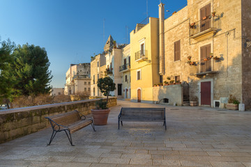 Fototapeta na wymiar View of a beautiful alley with two benches in front of buildings illuminated by the rising sun near the sea in Bari, Italy