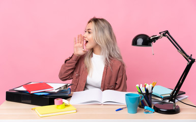 Young student woman working in a table shouting with mouth wide open