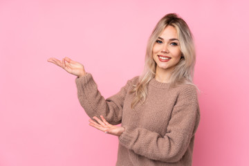 Teenager blonde girl wearing a sweater over isolated pink background extending hands to the side for inviting to come