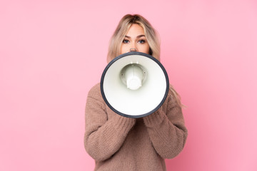 Teenager blonde girl wearing a sweater over isolated pink background shouting through a megaphone