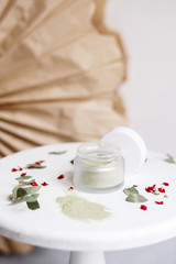 Fototapeta na wymiar Powder cosmetic mask. Glass jar with matcha on a white background with dry petals.