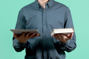 A teenager in a blue shirt is holding a tablet and a book in front of him, as if choosing one and...