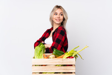 Farmer girl holding a basket full of fresh vegetables over isolated white background with arms...
