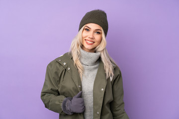 Teenager blonde girl with winter hat over isolated purple background laughing