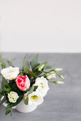 Spring bouquet in white vase on wooden white stand. Roses, tulips and lisianthus.