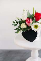 Black board heart copyspace. Spring bouquet in white vase on wooden white stand. Roses, tulips and lisianthus.
