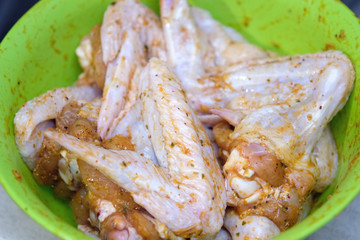 Chicken wings in a marinade in a green plastic bowl. Raw chicken wings in spices.