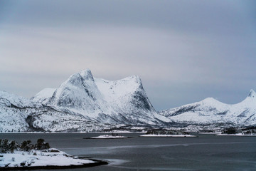 Spectacular winter landscape shoot in northern Norway. Mountains covered with snow near a fjord, overcast sky.