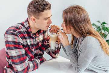 Woman and man drink coffee every morning at same place as tradition. They are drinking latte with straws from the same glass.