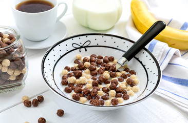 Wholegrain chocolate and milk balls, fruit, tea and milk on white wooden background. Healthy cereal breakfast. Baby breakfast. Baby eating. Balanced diet.