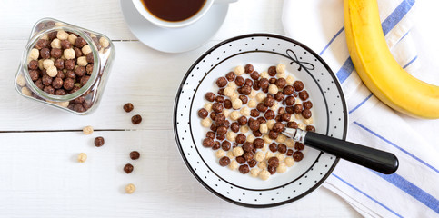 Wholegrain chocolate and milk balls, fruit, tea and milk on white wooden background. Healthy cereal breakfast. Baby breakfast. Baby eating. Balanced diet.