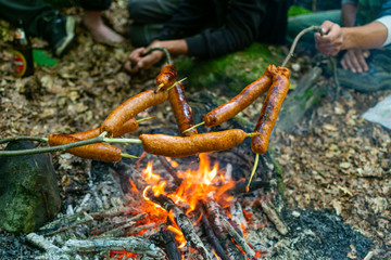Men baking bacons on camp fire in forest