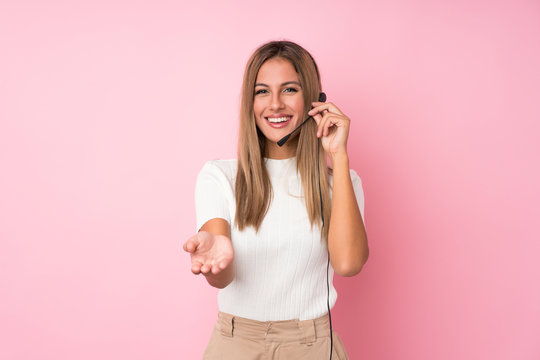 Young blonde woman over isolated pink background working with headset