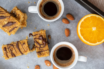Top view of raw vegan cookies on a tray next to oranges and two cups of coffee. Healthy no bake protein bar alternatives. Homemade plant based breakfast. Before and post workout snack.