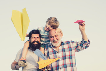 Grandfather, father and son are hugging and having fun together. Kid pilot with toy jetpack against...