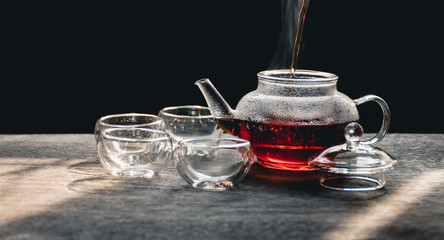 The steam from a cup or pot of tea on the old wood table and black background with nature light by window in the morning, Warm drinks make good healthy, Selective focus.