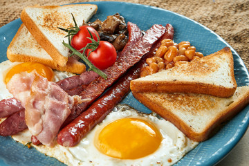 Classic English breakfast: toasts, smoked sausages, bacon, fried eggs, beans and fried toasts on a blue plate. Close up view. Food flat lay