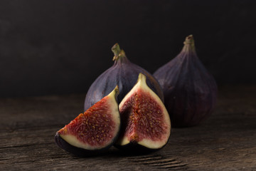 Fresh ripe figs. A few figs on an old wooden background. Whole figs and one fig sliced. Fresh fruits, purple figs on the wooden background. Autumn harvest. Free space for text. Free space for text. Da