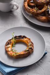 Pumpkin grill served on a plate. Baked pumpkin sliced rings with a knife, fork and napkin on a concrete table. Autumn dish. Halloween dish. Everyday autumn kitchen. Orange colors. space for text.  
