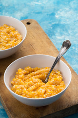 Pumpkin porridge. Homemade pumpkin porridge in a white plate on the table, ready to eat. Pumpkin cream soup or porridge in a bowl Blue table. Family breakfast. Free space for text. View from above.