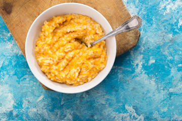 Pumpkin porridge. Homemade pumpkin porridge in a white plate on the table, ready to eat. Pumpkin cream soup or porridge in a bowl Blue table. Family breakfast. Free space for text. View from above. 