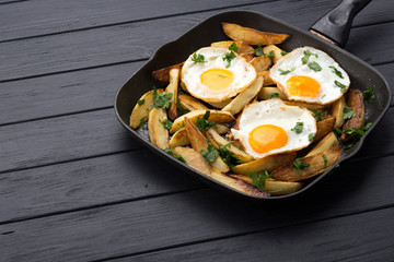 Breakfast in the pan. Fried potatoes with eggs in a skillet. Food bachelor. Cooked by a man. Hot and fresh. Homemade breakfast on black table. Fried eggs and sweet potato hash in cast iron skillet Fre