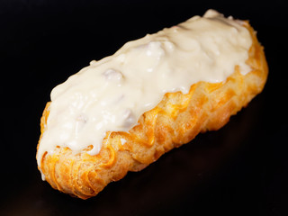 Eclair with white chocolate icing. One eclair against a dark background.