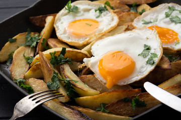 Breakfast in the pan. Fried potatoes with eggs in a skillet. Food bachelor. Cooked by a man. Hot and fresh. Homemade breakfast on black table. Fried eggs and sweet potato hash in cast iron skillet Fre