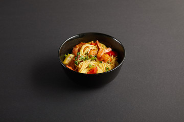 noodles with shrimps and vegetables in bowl on black background