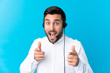 Telemarketer man working with a headset over isolated blue background points finger at you