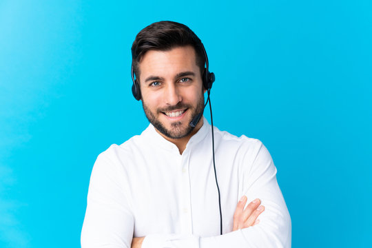 Telemarketer man working with a headset over isolated blue background laughing