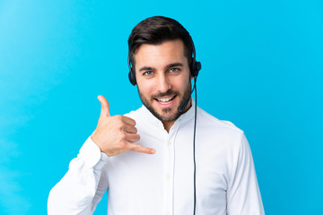 Telemarketer man working with a headset over isolated blue background making phone gesture - obrazy, fototapety, plakaty