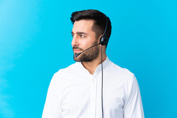 Telemarketer man working with a headset over isolated blue background looking to the side
