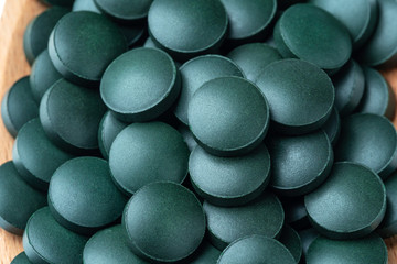 Vitamin and mineral supplements for vegetarians spirulina in tablets in a wooden spoon, close-up.