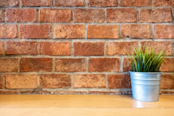 Plant in metal pot on wooden table  front of red brick wall background in coffee shop. Copy space for text or designed.