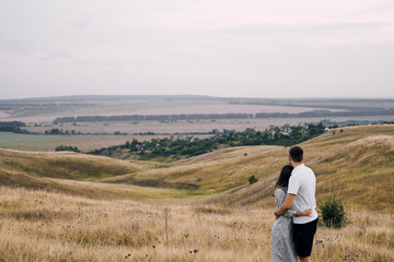 A young couple in love stands in a field on a hill and looks into the distance. Hug and admire the...