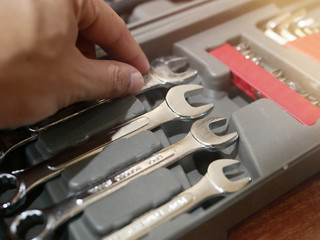 A man's hand is holding a wrench in various sizes in a toolbox.