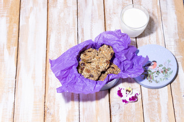 Oat vegan healthy cookies baked with banana, cereals and raisin in round box with violet wrapping paper and cap on wooden background, orchid flower, milk glass