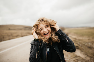 Portrait of young woman with hair blowing in the wind. She is  wearing a leather jacket with a...