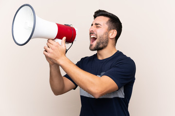Young handsome man with beard over isolated background shouting through a megaphone