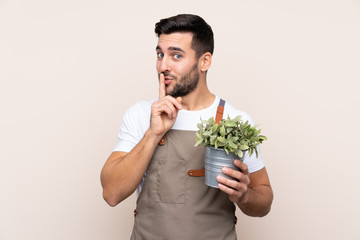 Gardener man holding a plant over isolated background doing silence gesture
