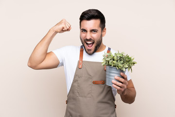 Gardener man holding a plant over isolated background celebrating a victory