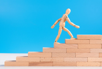 Fototapeta na wymiar Figure of wooden man climb up the stairs of success or career. Concept of career up, success in life, personal development and progress. Copy space for ad or text. Blue background. Long wooden bricks