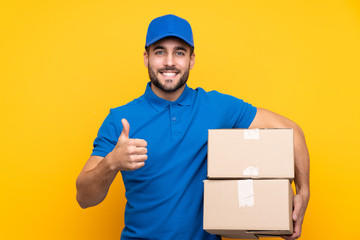 Delivery man over isolated yellow background with thumbs up because something good has happened - obrazy, fototapety, plakaty