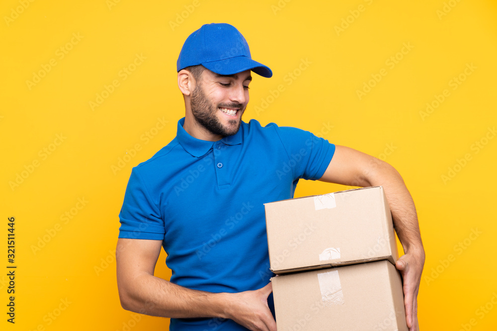 Wall mural delivery man over isolated yellow background with happy expression