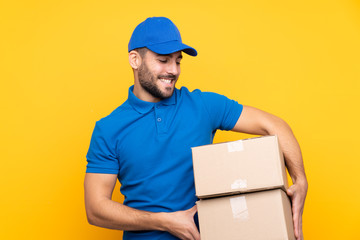 Delivery man over isolated yellow background with happy expression