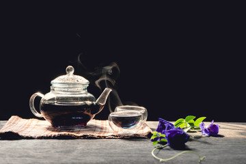 The steam from a cup or pot of tea on the old wood table and black background with nature light by window in the morning, Warm drinks make good healthy, Selective focus.