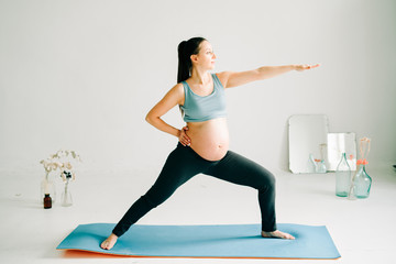 Fototapeta premium young beautiful pregnant girl in sportswear doing yoga, doing asana Virabhadasana-Warrior Pose on the Mat in the Studio
